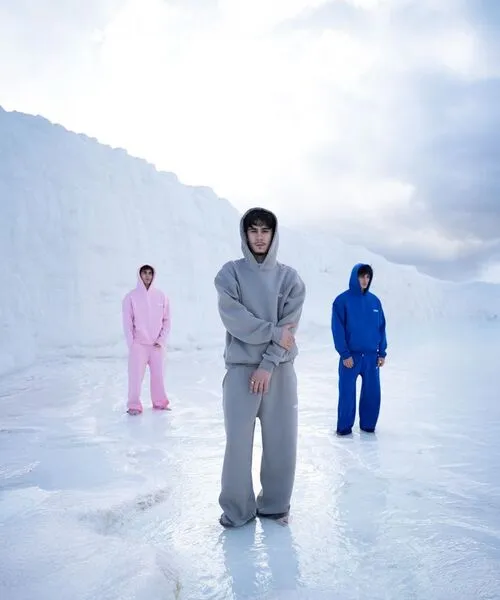 Three models standing in a snowy landscape wearing oversized matching hoodie and track pane sets in grey, pink, and bright blue colors, showcasing premium winter streetwear.