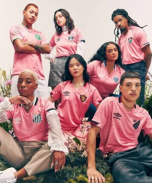 A diverse group of models posing outdoors in matching light pink short-sleeved jerseys featuring subtle geometric textures and athletic crests.