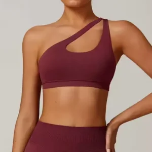 A woman wearing a deep maroon one-shoulder sports bra featuring a unique diagonal strap and a stylish triangular cut-out detail on the chest.