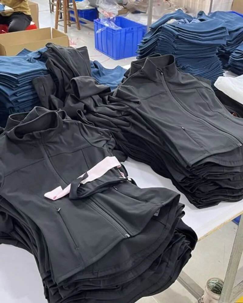 Neatly folded stacks of black zip-up athletic top and leggings with high collars on a habit fit sports factory table, showcasing bulk garment manufacturing of performance activewear.