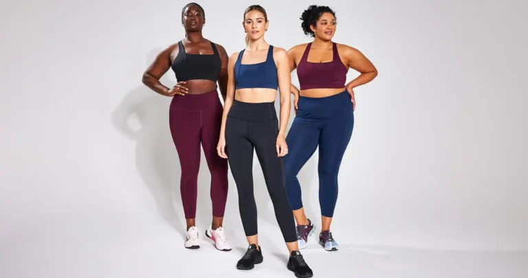 Three women of diverse body types standing together in athletic wear; one wears a black sports bra with burgundy leggings, the middle wears a navy blue set, and the third wears a burgundy sports bra with navy leggings.