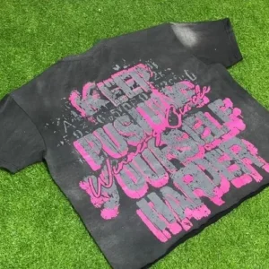 A black acid-wash custom t-shirt featuring a bold pink "KEEP PUSHING YOURSELF HARDER" graphic screen print, showcasing a vintage textured finish.