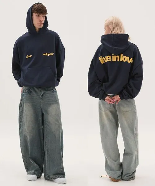 A front and back view of a navy blue oversized streetwear hoodie featuring yellow "anilopeer" branding on the chest and a bold "live in love" slogan on the back; paired with extra-wide baggy acid-wash denim jeans and white sneakers for a modern urban aesthetic.
